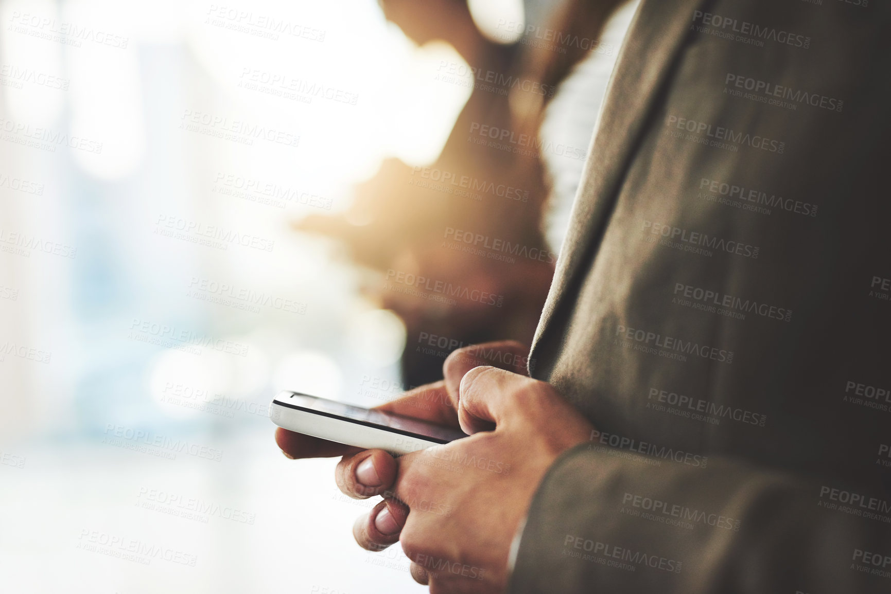 Buy stock photo Shot of a businessperson using his cellphone with colleagues blurred in the background