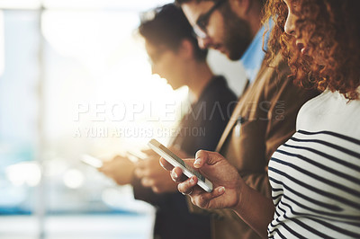 Buy stock photo Shot of a businessperson using her cellphone with colleagues blurred in the background