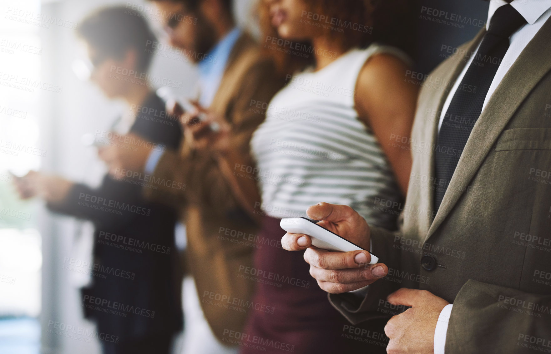 Buy stock photo Shot of a businessperson using his cellphone with colleagues blurred in the background