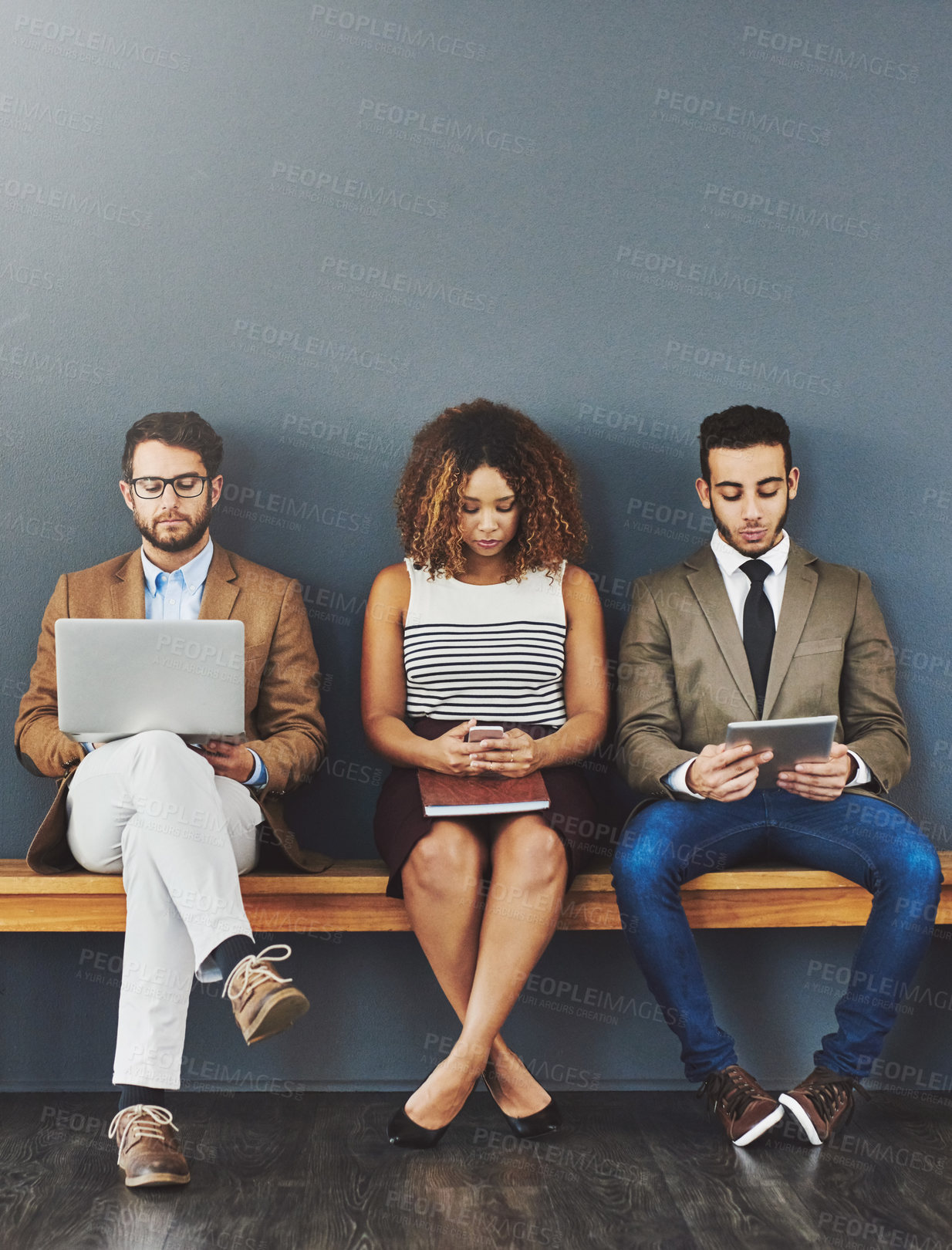 Buy stock photo Group of design interns on wireless online devices waiting at a job interview of a startup company. Diverse people sitting, waiting for a meeting with human resources for a job