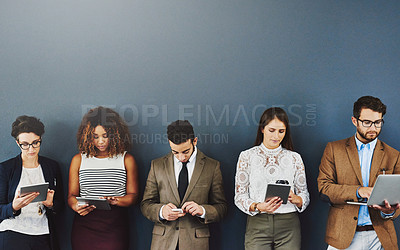 Buy stock photo Group of businesspeople texting, typing and browsing online while waiting and standing in line on grey studio wall. Diverse team using tablet, laptop and phone and holding different wireless gadgets