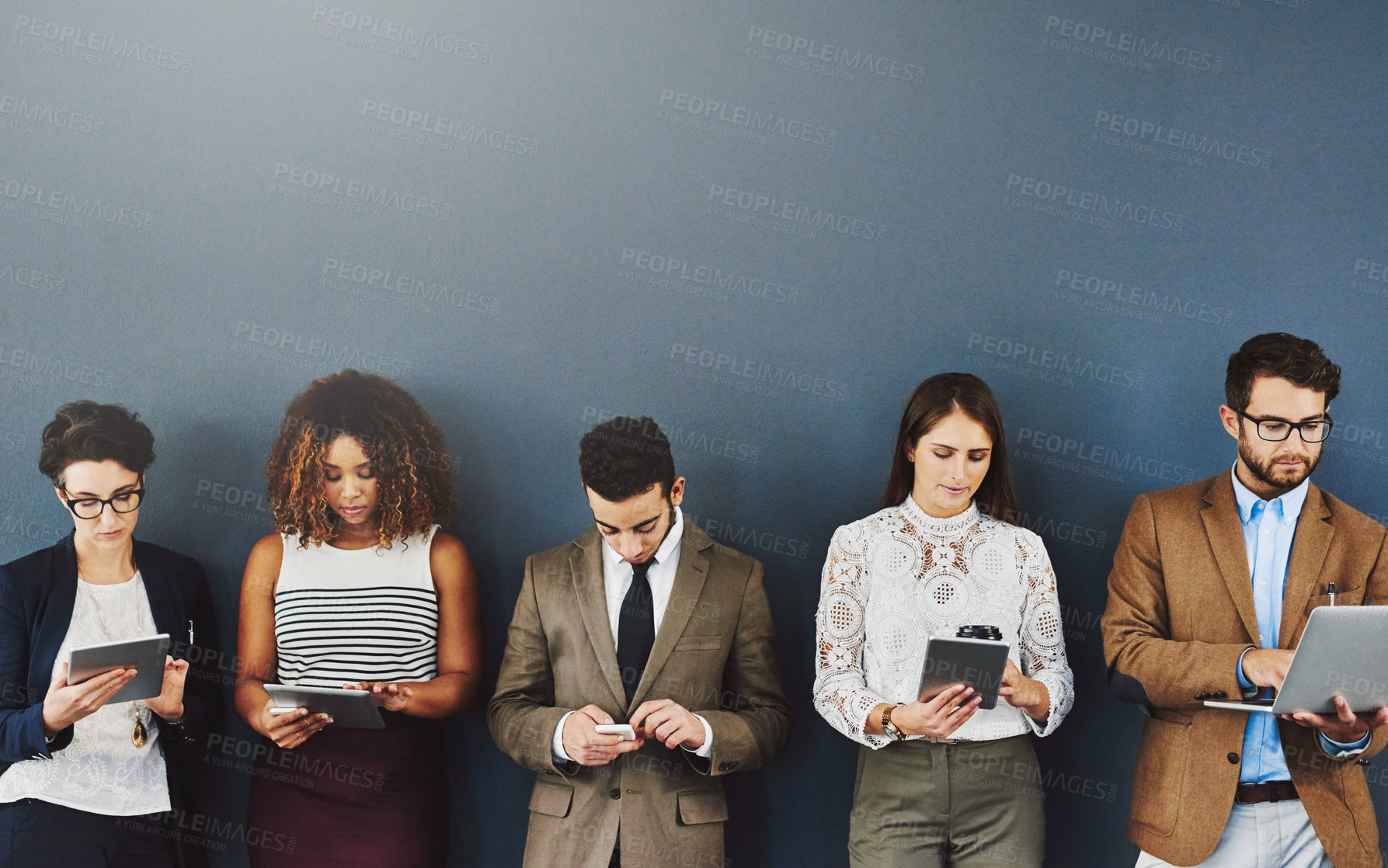 Buy stock photo Group of businesspeople texting, typing and browsing online while waiting and standing in line on grey studio wall. Diverse team using tablet, laptop and phone and holding different wireless gadgets