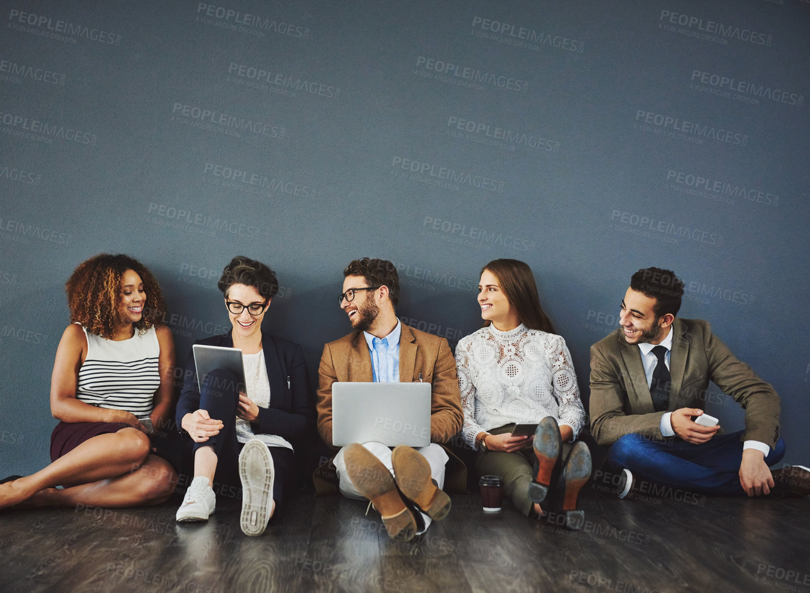 Buy stock photo Studio shot of a group of businesspeople using wireless technology and talking on the floor against a gray background