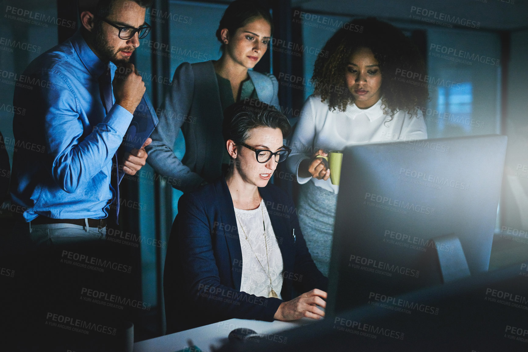 Buy stock photo Shot of colleagues standing together as they work on something on a computer at night