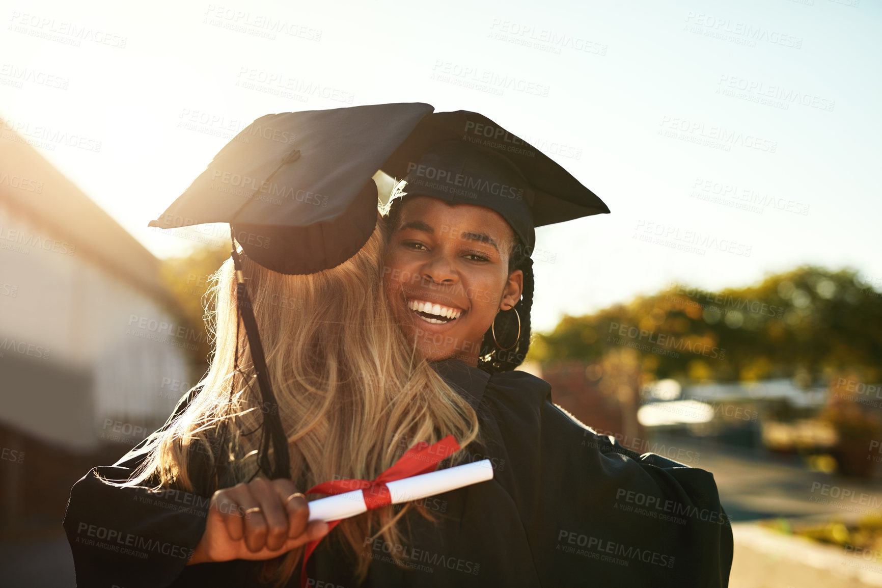 Buy stock photo Shot of two happy young women hugging on graduation day