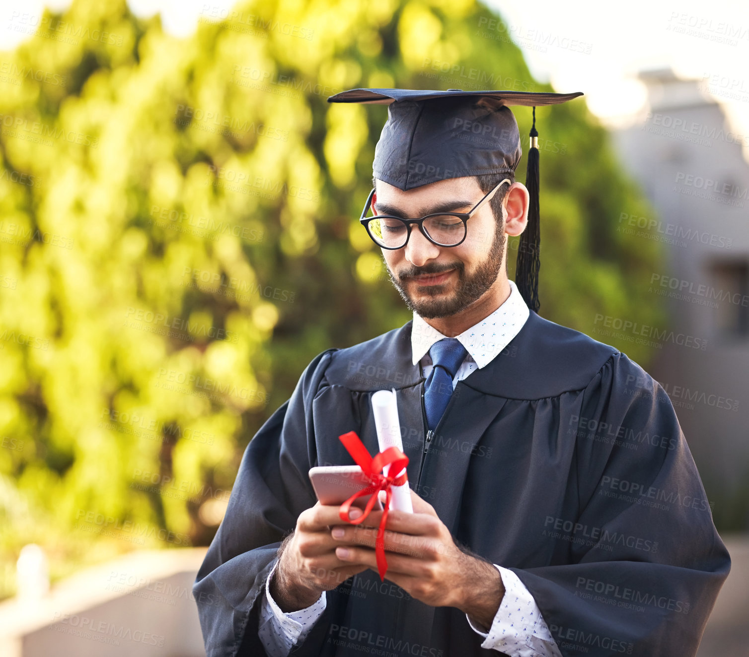 Buy stock photo Shot of a young man using a mobile phone on graduation day
