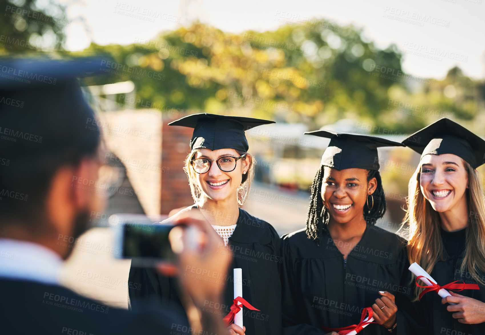 Buy stock photo Phone, students and graduation picture in outdoor, diploma celebration and photography memory. People, friends and certified together for university success, social media post and women for victory