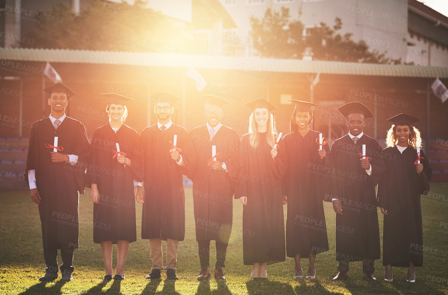 Buy stock photo Graduation, campus or portrait of students with sunrise at university for education, learning or success. College, diploma or happy people in group with degree, flare or certificate for empowerment