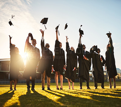 Buy stock photo Shot of a group of smiling university students cheering and throwing their caps outside on graduation day