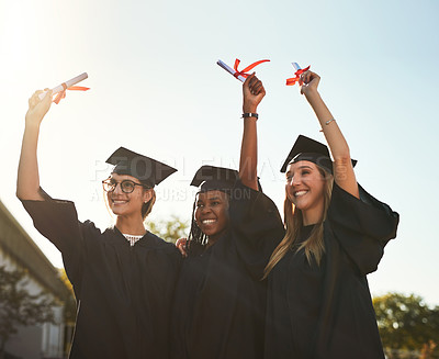 Buy stock photo Shot of university students holding up their diplomas on graduation day