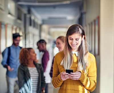 Buy stock photo Cropped shot of an attractive young female university student using her cellphone while walking through the campus corridor