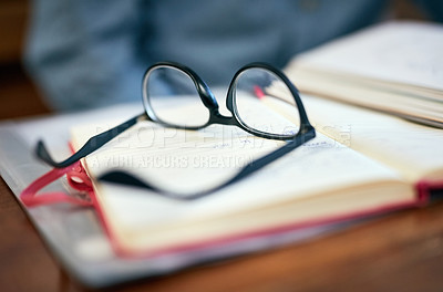 Buy stock photo Closeup shot of reading glasses on an open book on a university desk indoors