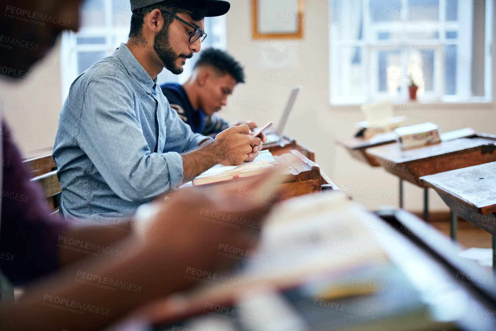 Buy stock photo Man, classroom and college with phone for research, reading message on mobile app at school. Male student, university or social media with education or learning, scroll for news story with glasses