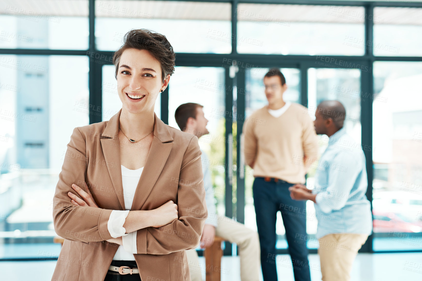 Buy stock photo Portrait of a designer standing with her arms crossed with colleagues blurred in the background