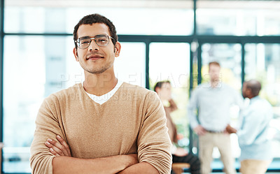 Buy stock photo Portrait of a designer standing with his arms crossed with colleagues blurred in the background