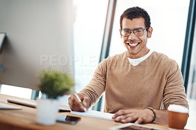 Buy stock photo Portrait of a young designer writing notes while working at his desk in an office