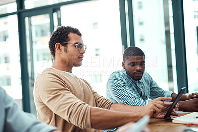 Buy stock photo Shot of two young designers working on a digital tablet in an office