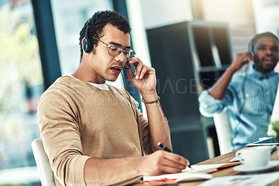 Buy stock photo Cropped shot of a call center agent sitting at his desk with his colleague blurred in the background