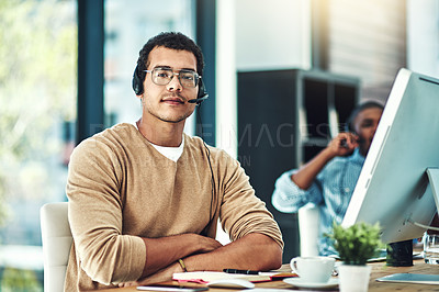 Buy stock photo Cropped shot of a call center agent sitting at his desk with his colleague blurred in the background