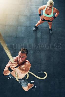 Buy stock photo Shot of a young man climbing a rope with a woman in the background at the gym