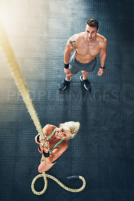Buy stock photo Shot of a young woman climbing a rope with a man in the background at the gym