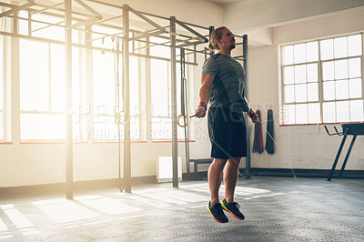 Buy stock photo Shot of a muscular young man training with a skipping rope at the gym
