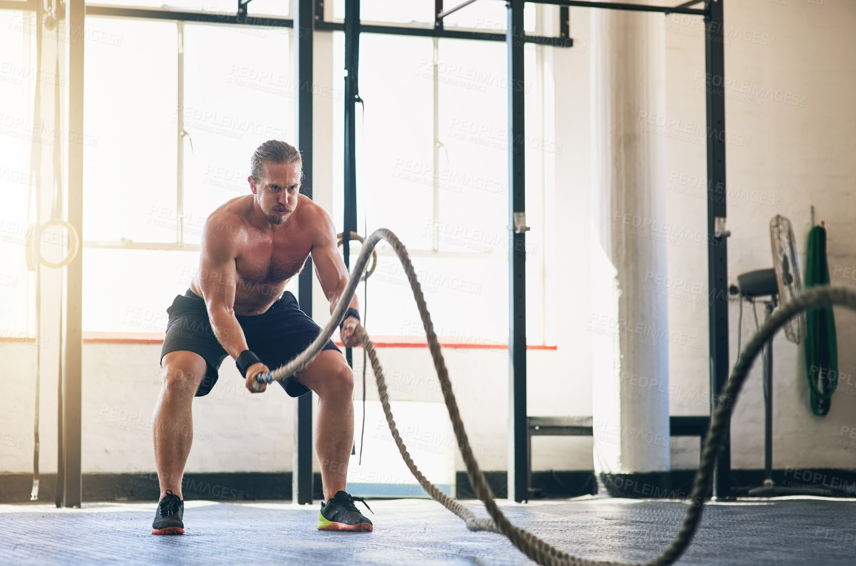 Buy stock photo Shot of a muscular young man working out with heavy ropes at the gym