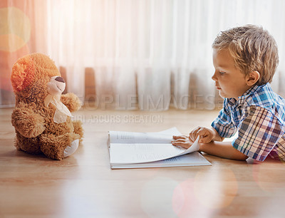 Buy stock photo Shot of a little boy lying on the floor with a book and his teddybear