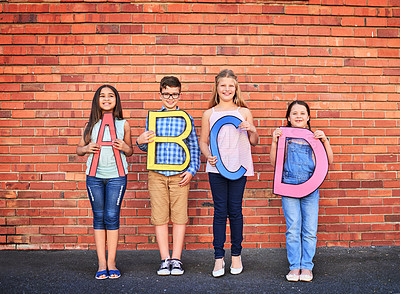 Buy stock photo Portrait of a group of young children holding letters from the alphabet against a brick wall