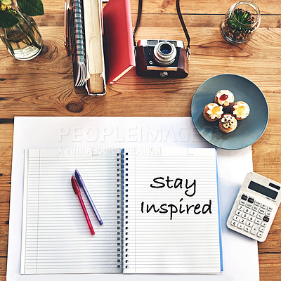 Buy stock photo Shot of a creative workstation with a notebook that has the words “stay inspired”written on it