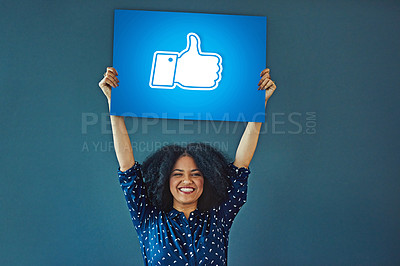 Buy stock photo Portrait, social media and thumbs up icon to like with a woman holding a poster in studio on a blue background. Smile, logo and button with a happy female influencer showing a hand gesture sign