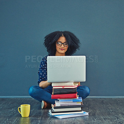 Buy stock photo Studio shot of a young woman using a laptop with books stacked in front of her against a gray background