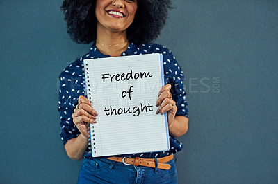 Buy stock photo Studio shot of a young woman holding a notebook with “freedom of thought” written on it against a gray background