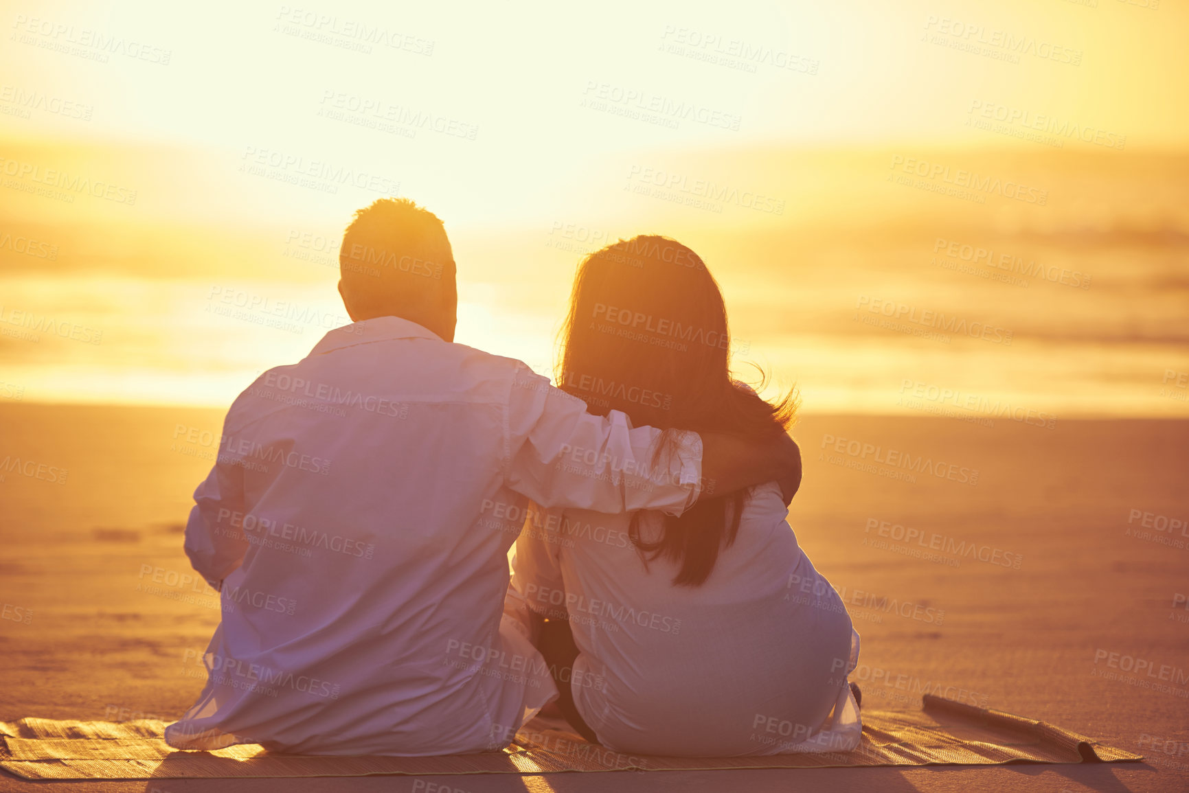 Buy stock photo Rearview shot of an affectionate mature couple enjoying the sunset while sitting on the beach