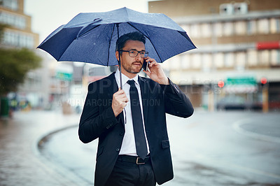 Buy stock photo Shot of a mature businessman talking on a cellphone and holding an umbrella while out in the city