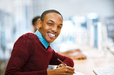 Buy stock photo Shot of a cheerful young man making notes while being seated in a library and looking at the camera