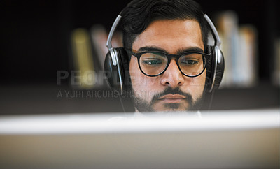 Buy stock photo Closeup shot of a focused young man sitting and working on a computer in a library while listening to music