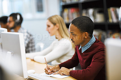 Buy stock photo Shot of a group young students working on computers and making notes in a library