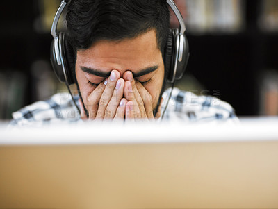 Buy stock photo Closeup shot of a stressed out young man working on a computer while listening to music with his eyes closed