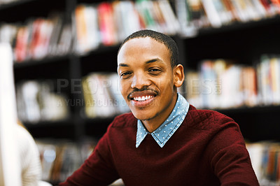 Buy stock photo Shot of a cheerful young man working on a computer while being seated in a library and looking at the camera