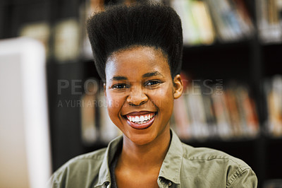 Buy stock photo Shot of a cheerful young woman working on a computer in a library while looking at the camera