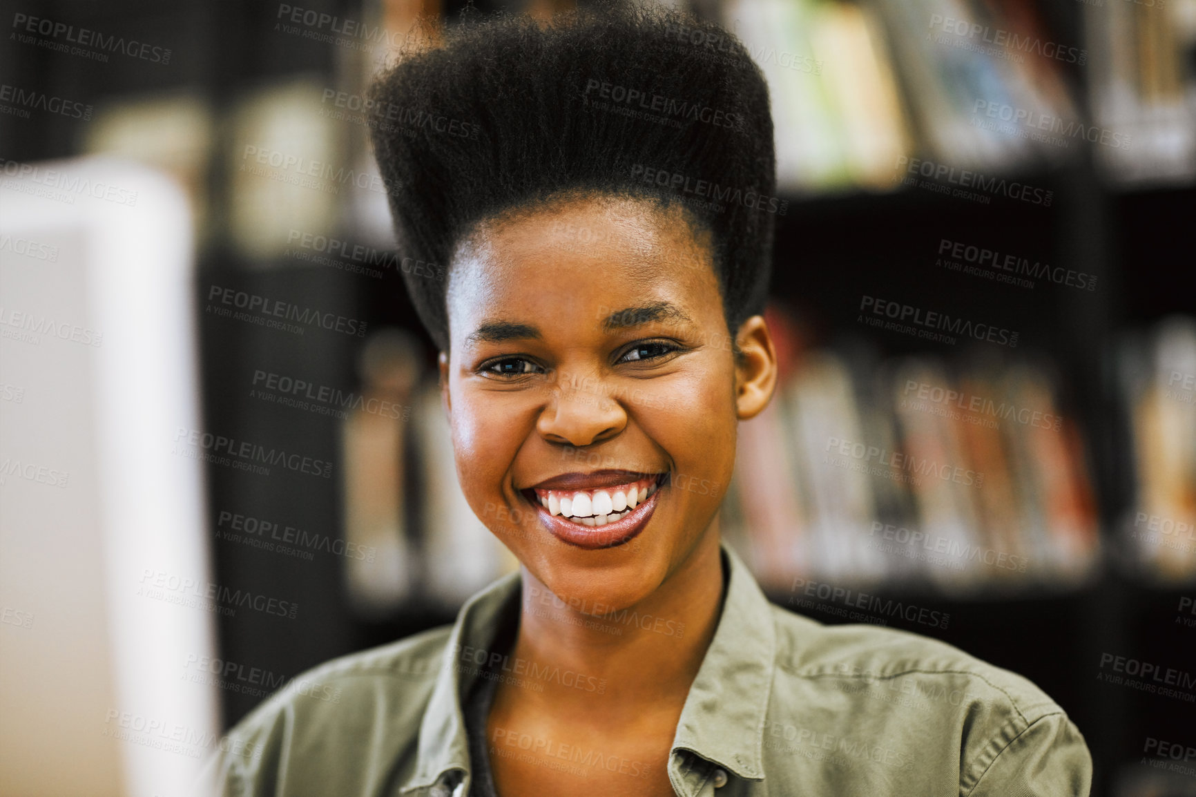 Buy stock photo Shot of a cheerful young woman working on a computer in a library while looking at the camera