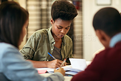 Buy stock photo Shot of a group of young students working together and making notes while being seated around a table