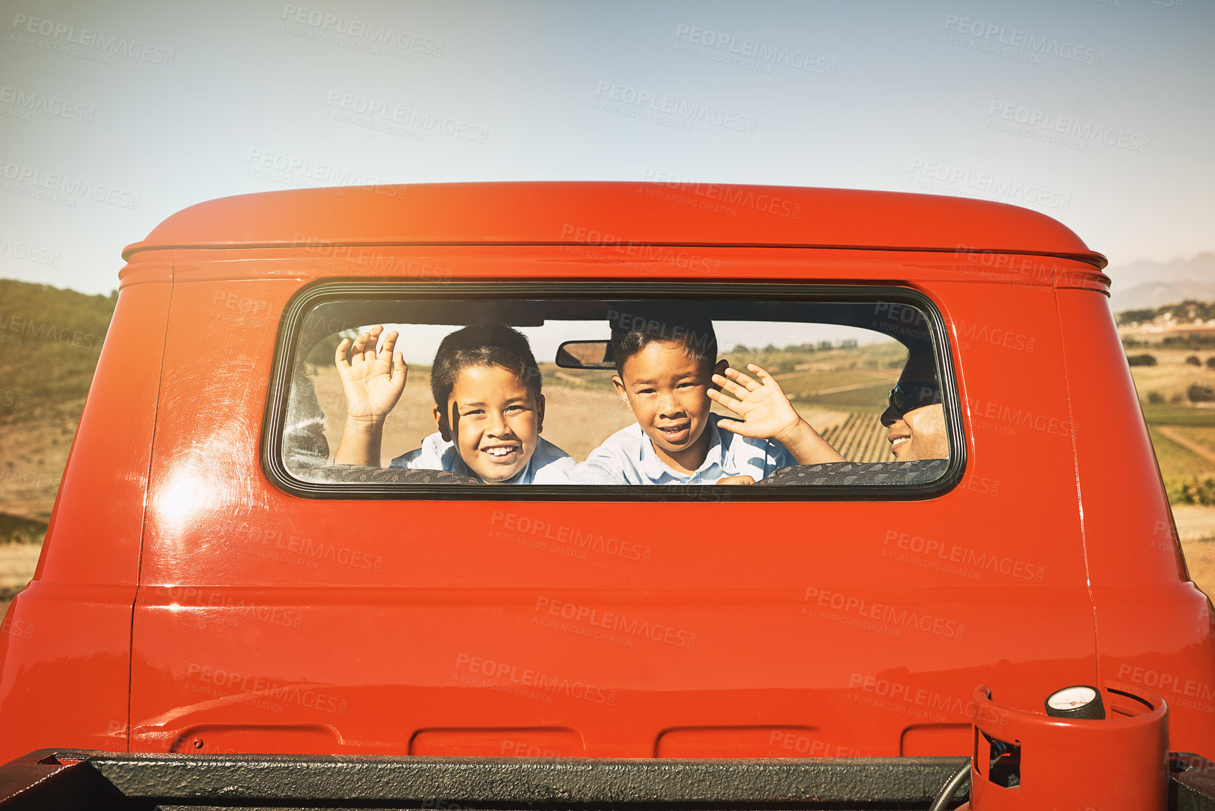 Buy stock photo Shot of two young cheerful boys smiling and waving from the back of a red pickup truck while looking into the camera