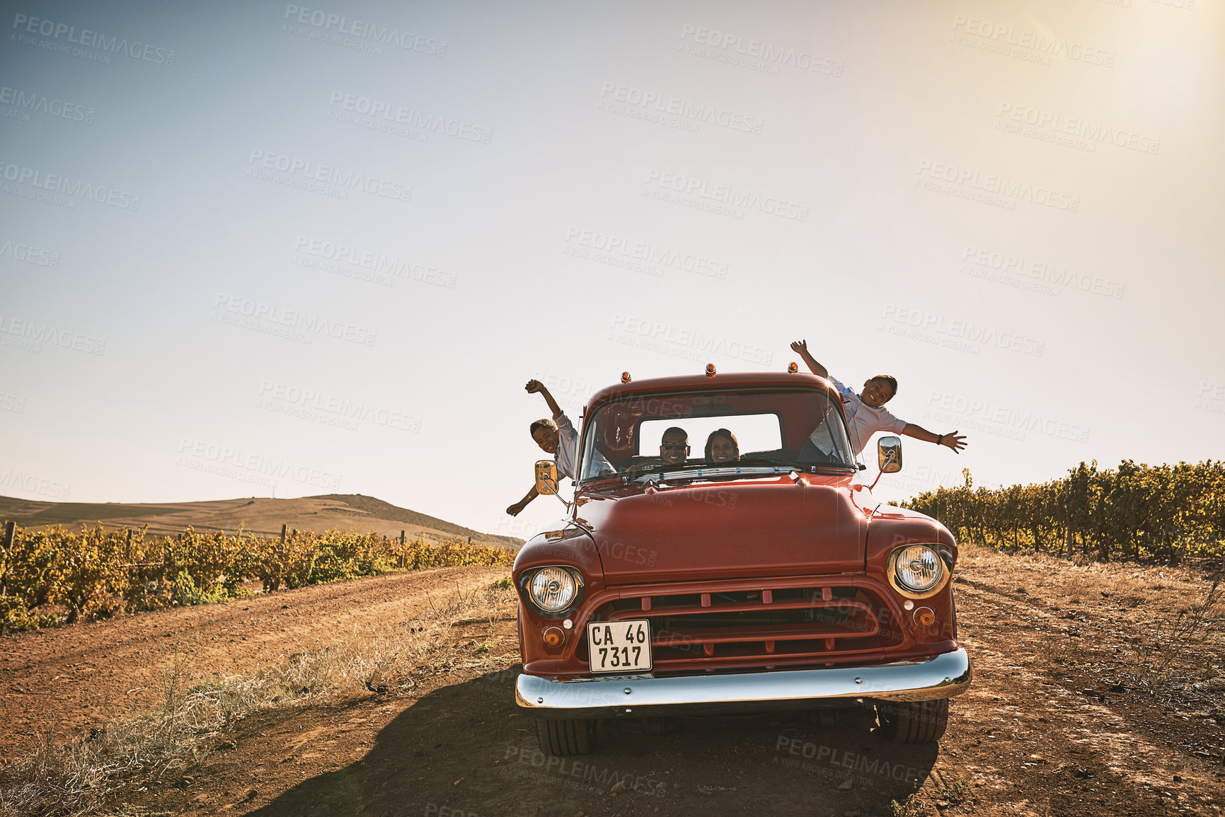 Buy stock photo Shot of a cheerful young family driving in a red pickup truck on a rural road outside