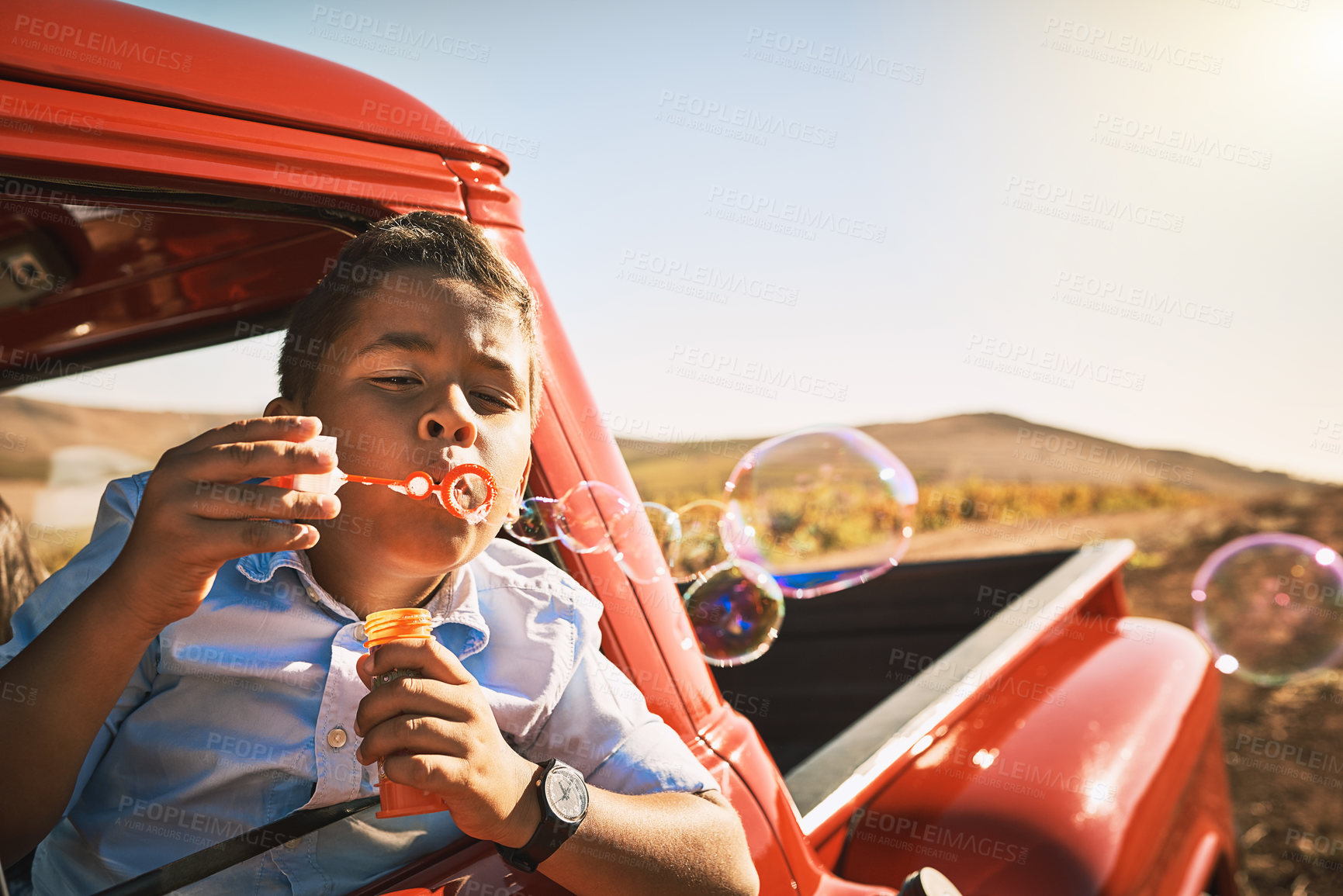 Buy stock photo Shot of a young cheerful boy blowing bubbles while being seated in a red pickup truck outside