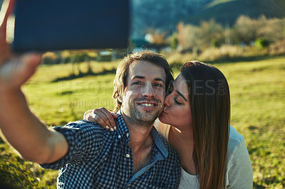 Buy stock photo Shot of an affectionate young couple taking a selfie together outdoors