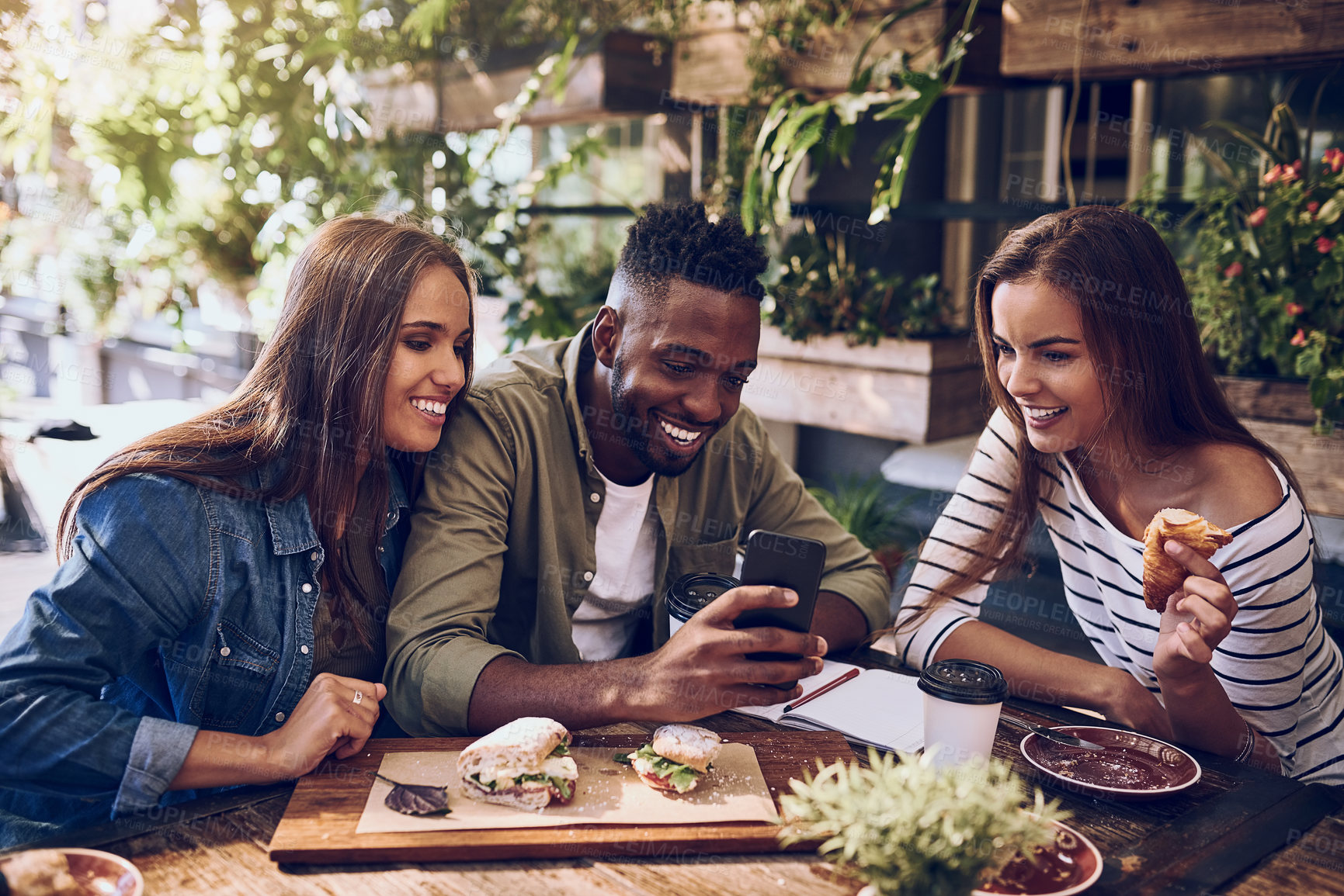 Buy stock photo Shot of three friends looking at something on a cellphone while out for lunch