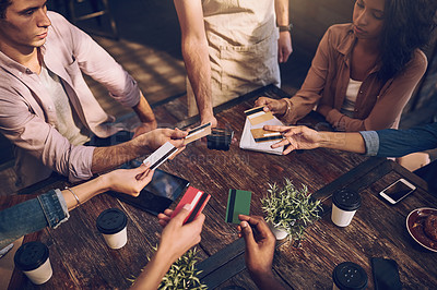 Buy stock photo High angle shot of a group of friends offering their bank cards to pay the bill at a cafe