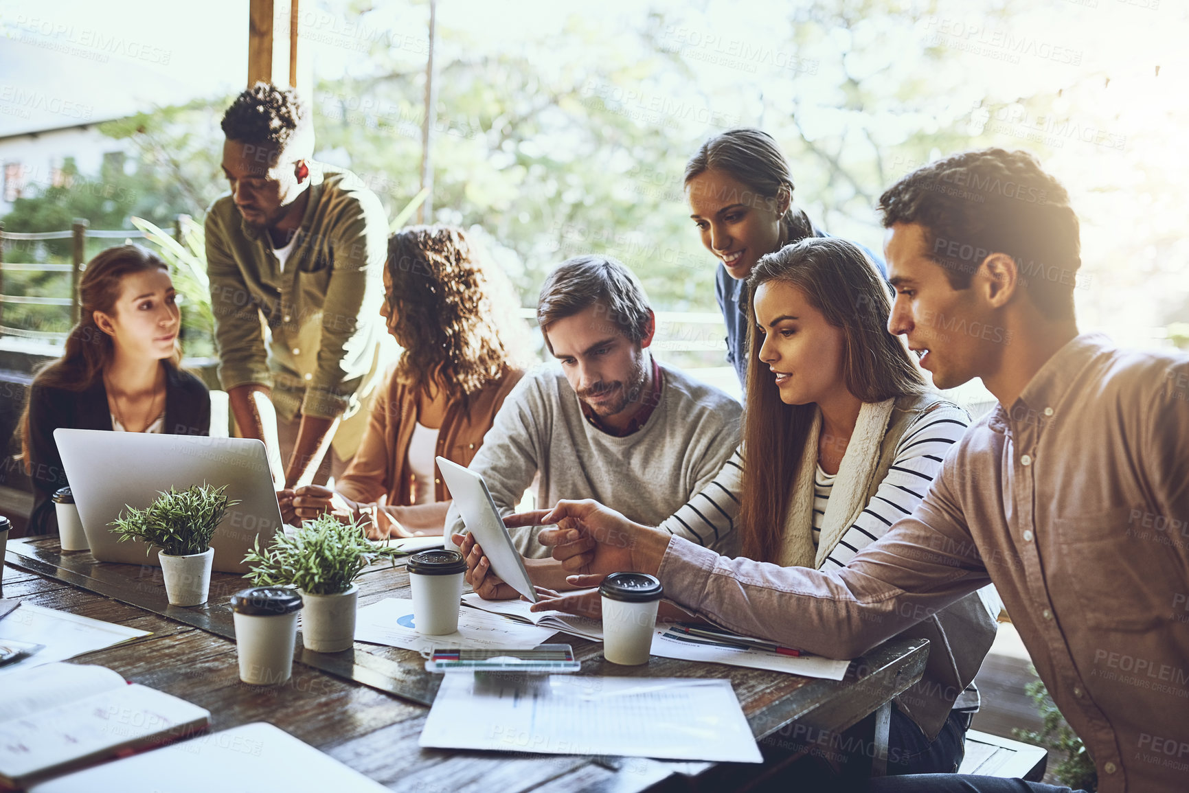 Buy stock photo Shot of a team of colleagues using a digital tablet and laptop together during a meeting at an outdoor cafe